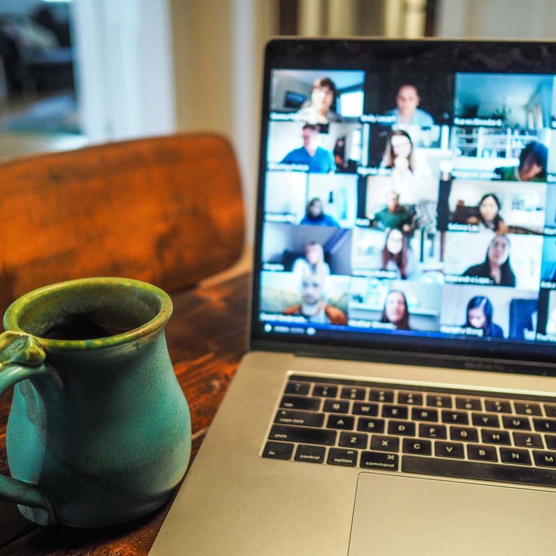 Photo of a laptop computer with a Zoom meeting on the screen and a coffee cup to the left of the keyboard