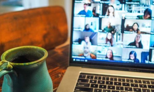 Photo of a laptop computer with a Zoom meeting on the screen and a coffee cup to the left of the keyboard