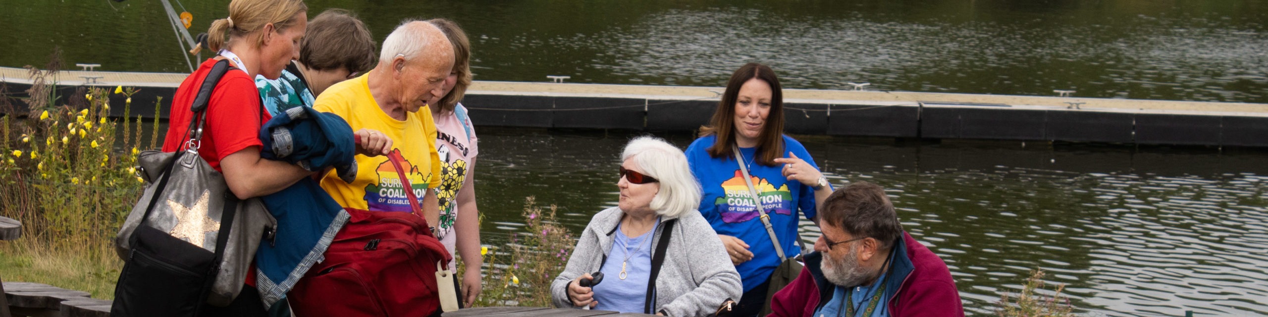 Members and staff gathering around a table and bench next to a lake