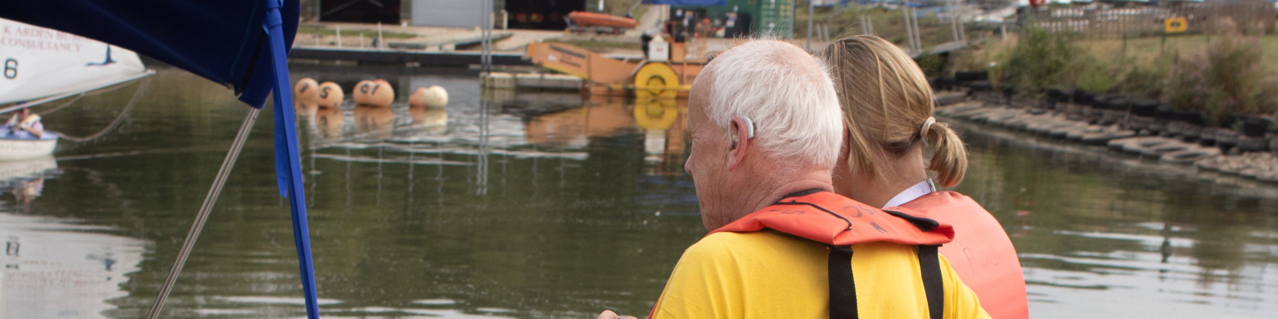 A member with a hearing aid with a member of staff boarding a sailing boat