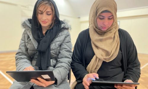 Two people sitting on chairs looking at digital tablets