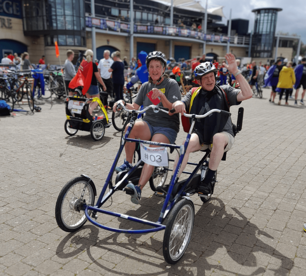 Coalition Chair Jonathan waving and staff member Caroline smiling on a side by side tandem bike