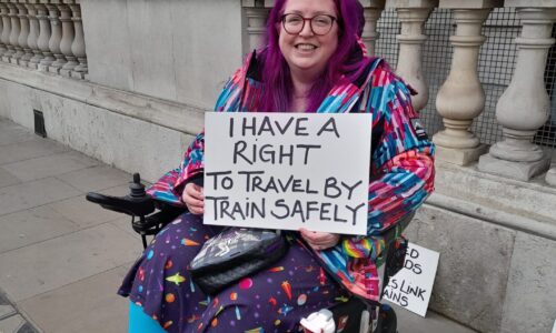 Vikki, the Coalition's Co-chair is a wheelchair user and is holding a sign that says 'I have a right to travel by train safely'.