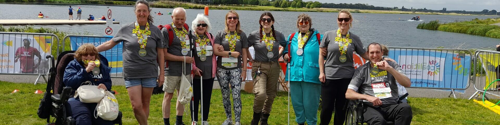 Group photo of members and staff smiling in front of a lake at the Superhero Tri event