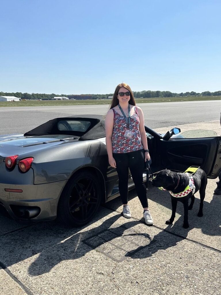 Megan next to a Ferrari with assistance dog Rowley 