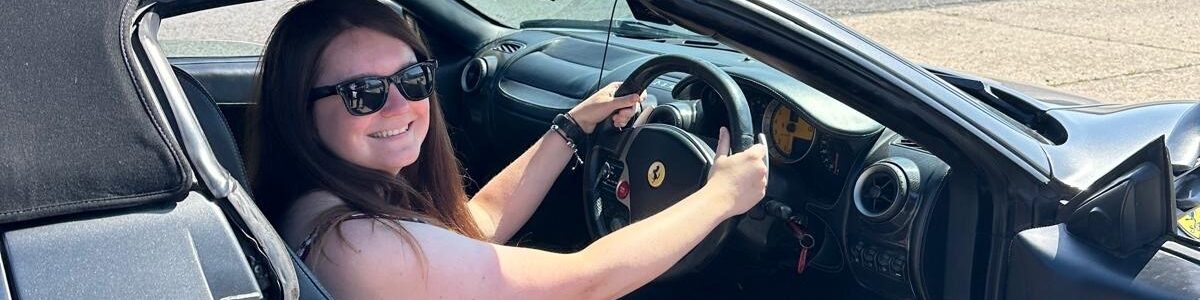 Megan smiling and sat in the drivers seat of a Ferarri.