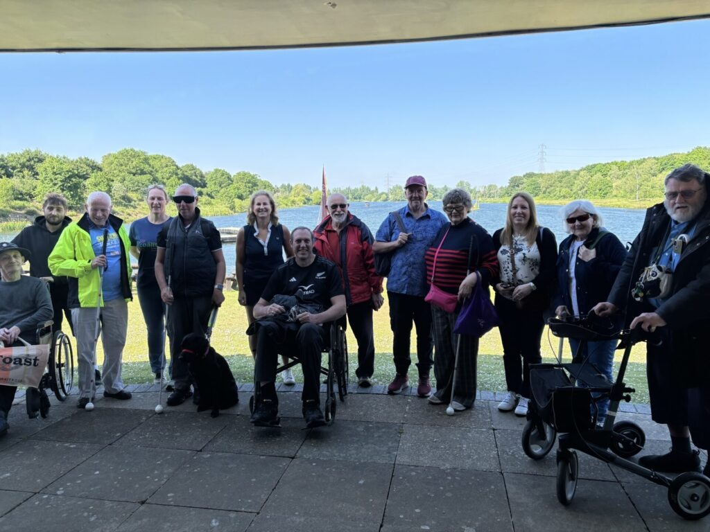 Group photo of Coalition members and staff in front of a sailing lake on a sunny day.  