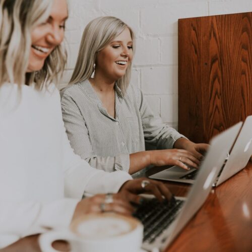 Two woman smiling whilst typing on laptops.