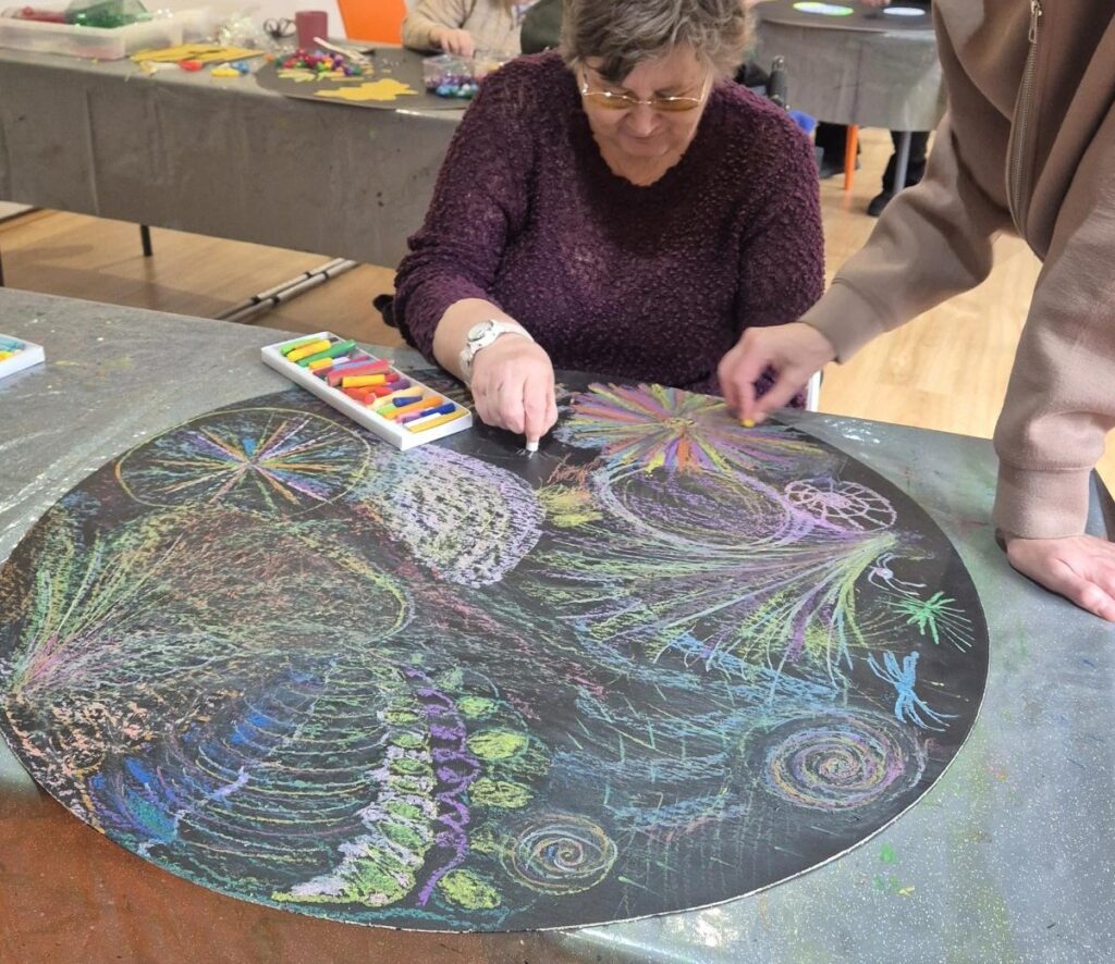 Coalition member Jane drawing on a circular black chalk board with colourful fireworks and patterns.