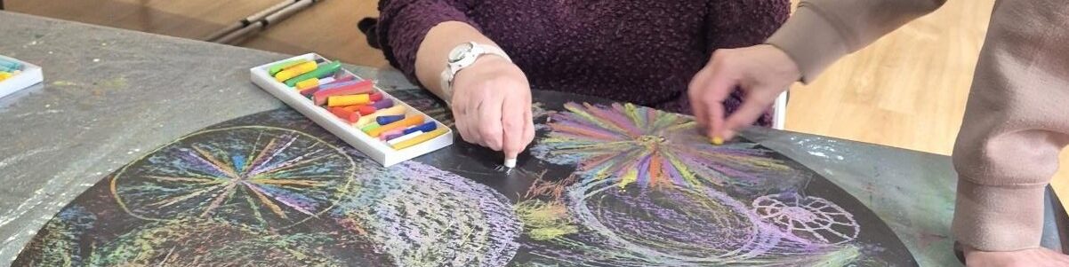 Coalition member Jane drawing on a circular black chalk board with colourful fireworks and patterns.
