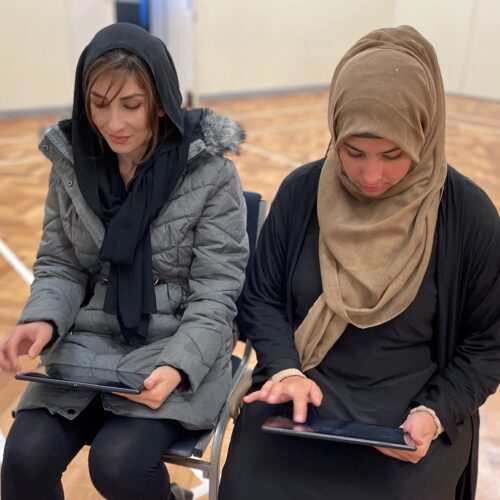 Two woman looking at digital tablet devices.