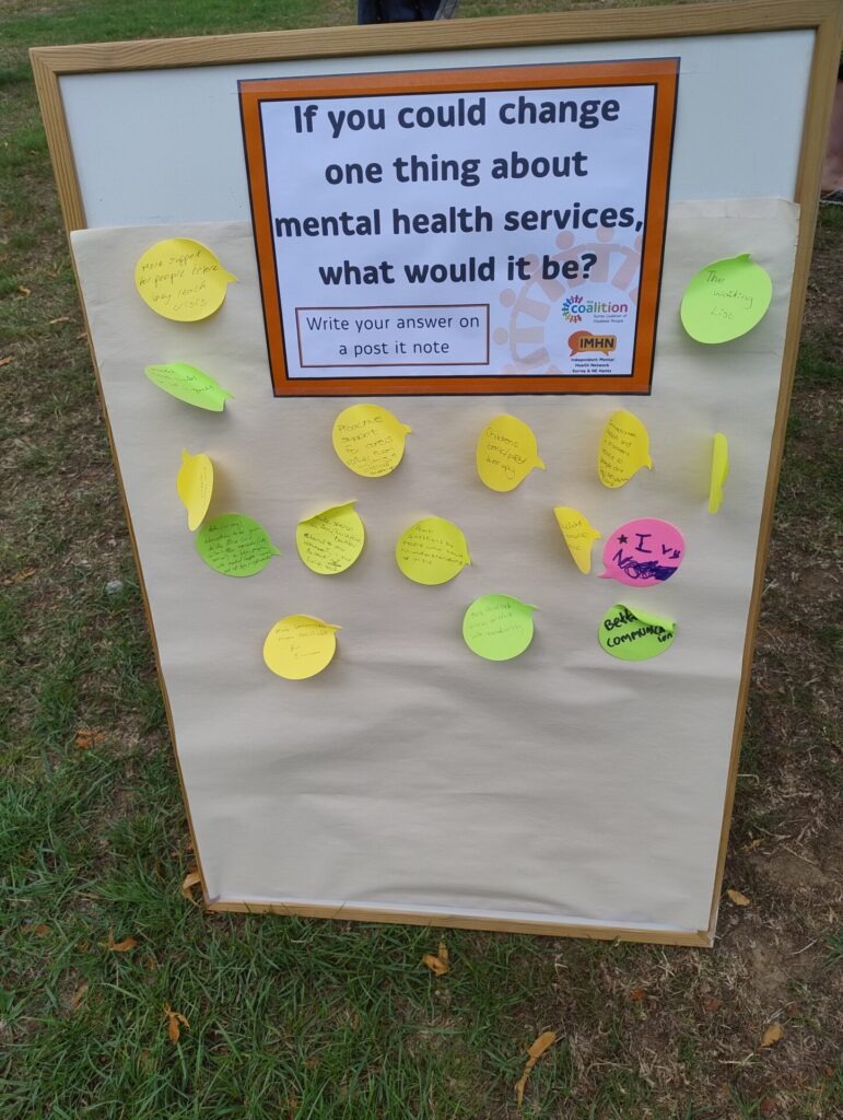 Board with the title 'If you could change one thing about mental health services what would it be? ' below this are several sticky notes with people's comments