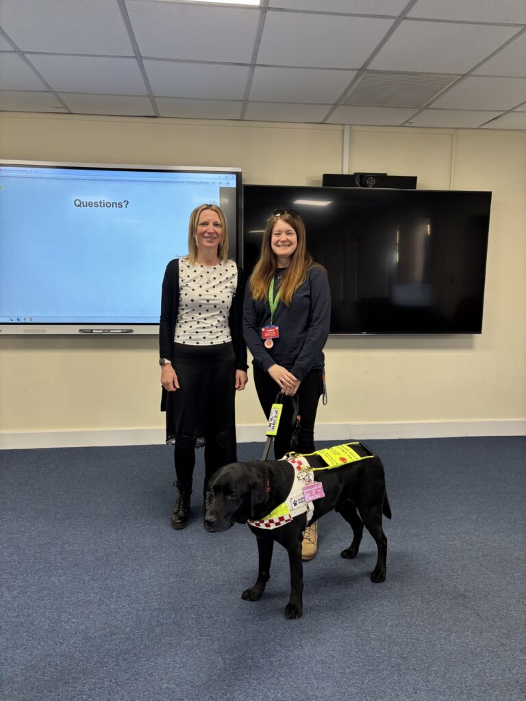 Coalition CEO Nikki with Involvement Officer Megan and her assistance dog, Rowley in front of a digital board that says 'questions?'.