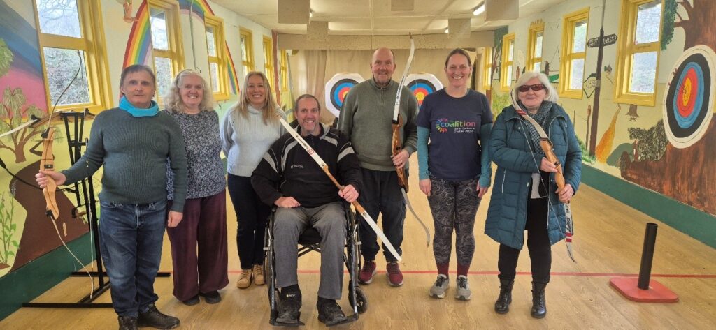 Coalition members and staff with archery bows and targets in the background.